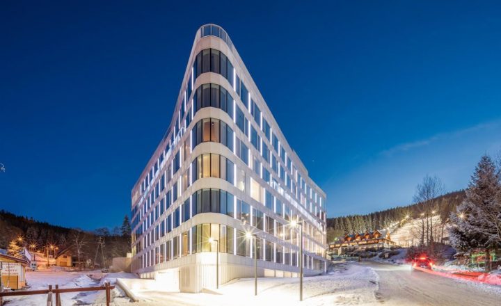 A well-lit hotel building in a triangular form of architecture, standing out in a winter forest background